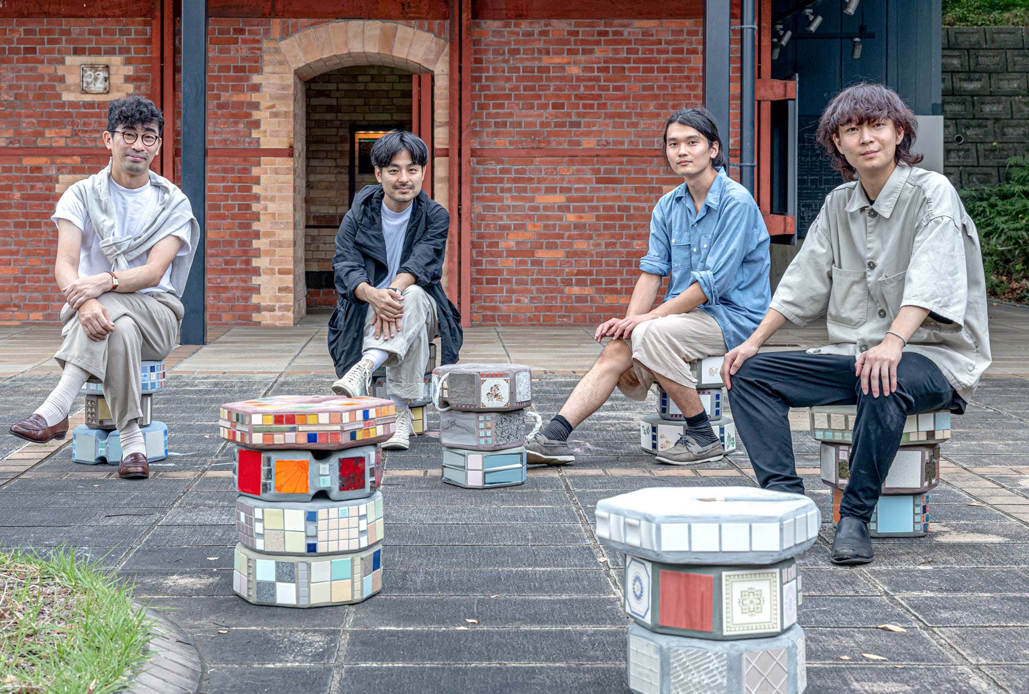 東京藝術大学 中山研究室　左から中山准教授、湯浅助手、藤井さん、岩崎さん　完成した「タイルアートの重石」のスツールに座るみなさん。