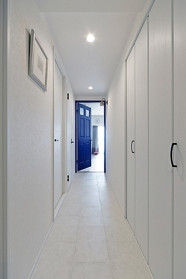 白いフロアタイルの廊下の先、青いドアがアクセント。の写真
